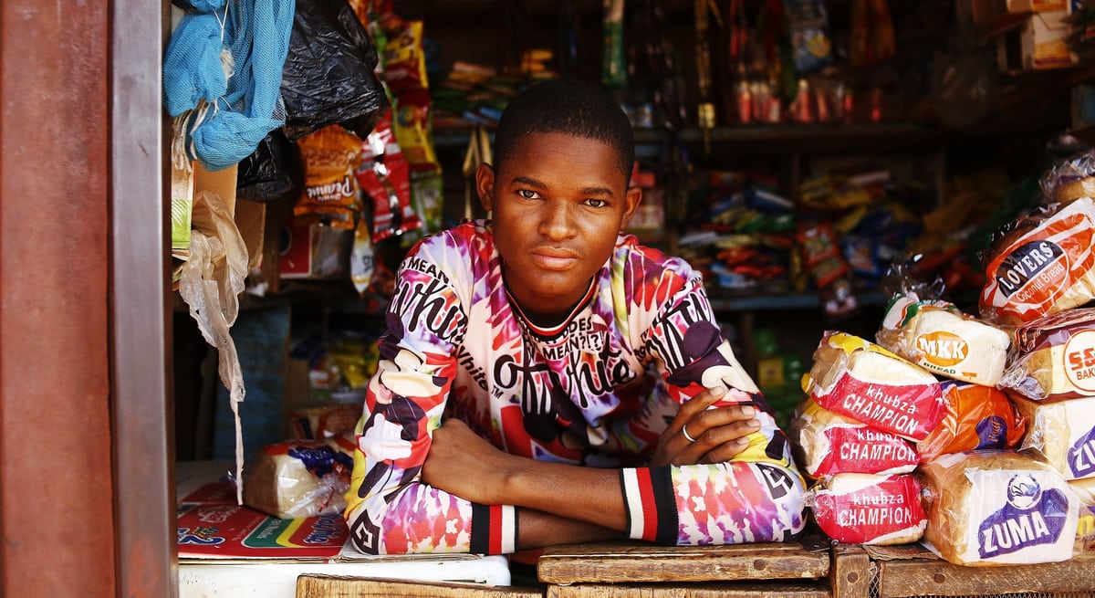 Shop owner at the counter of his provision store, stocked shelves behind him